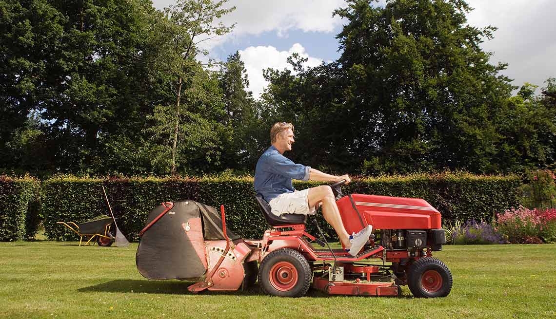 Hombre conduce una podadora de cesped - Consejos para la limpieza de primavera y el mantenimiento del patio